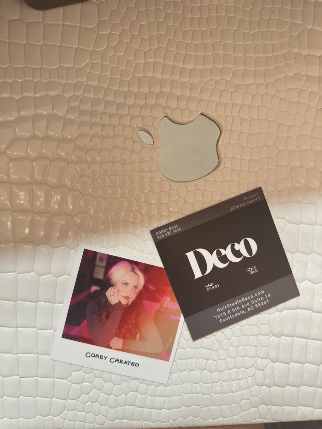A Deco business card and a Corey Created polaroid on a cream croc surface
